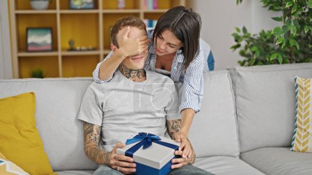 Téléchargez les photos : Beau couple souriant confiant surprise avec cadeau à la maison - en image libre de droit