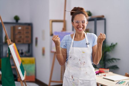 Photo for Brunette woman painting at art studio screaming proud, celebrating victory and success very excited with raised arms - Royalty Free Image