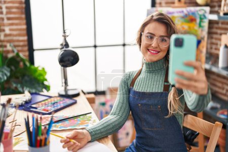 Téléchargez les photos : Young woman artist smiling confident making selfie by smartphone at art studio - en image libre de droit
