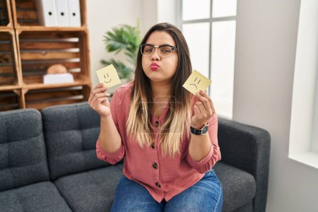 Photo for Young hispanic woman holding sad to happy emotion paper puffing cheeks with funny face. mouth inflated with air, catching air. - Royalty Free Image