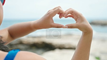 Foto de Joven turista china vistiendo bikini haciendo gesto de corazón en la playa - Imagen libre de derechos