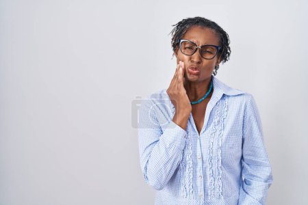 Téléchargez les photos : Femme africaine avec dreadlocks debout sur fond blanc portant des lunettes touchant la bouche avec la main avec une expression douloureuse en raison de maux de dents ou de maladies dentaires sur les dents. dentiste - en image libre de droit