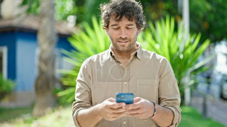 Photo for Young hispanic man smiling confident using smartphone at park - Royalty Free Image