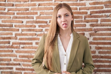 Photo for Young caucasian woman standing over bricks wall background sticking tongue out happy with funny expression. emotion concept. - Royalty Free Image