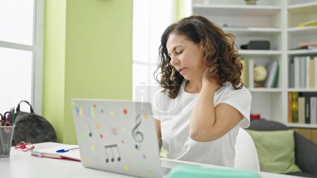 Photo for Middle age hispanic woman student using computer stressed for cervical pain at library university - Royalty Free Image