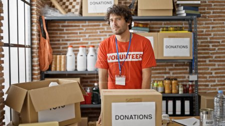 Téléchargez les photos : Jeune homme hispanique bénévole debout par des dons boîte en carton au centre de charité - en image libre de droit