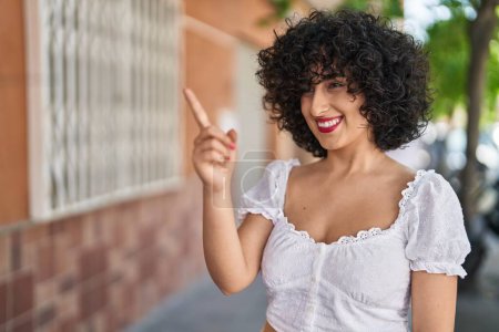 Téléchargez les photos : Jeune femme du Moyen-Orient souriant confiant pointant du doigt dans la rue - en image libre de droit
