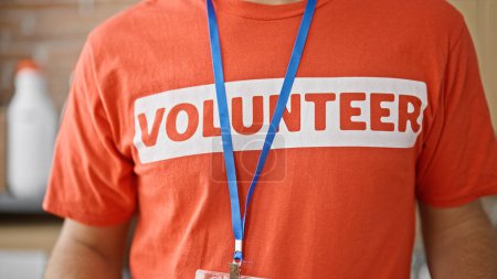 Téléchargez les photos : Jeune homme hispanique portant un uniforme de bénévole debout au centre de bienfaisance - en image libre de droit