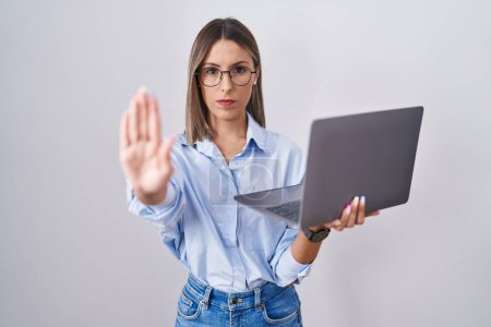 Photo for Young woman working using computer laptop doing stop sing with palm of the hand. warning expression with negative and serious gesture on the face. - Royalty Free Image