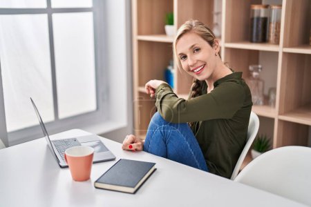 Téléchargez les photos : Jeune femme blonde utilisant un ordinateur portable boire du café à la maison - en image libre de droit