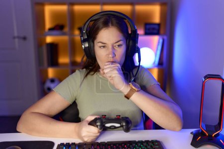 Téléchargez les photos : Belle femme brune jouant à des jeux vidéo portant des écouteurs se sentant mal et toussant comme symptôme de rhume ou de bronchite. concept de soins de santé. - en image libre de droit
