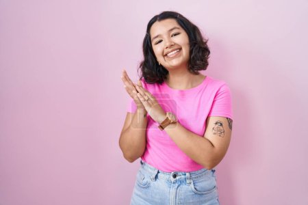 Foto de Joven mujer hispana de pie sobre fondo rosa aplaudiendo y aplaudiendo felices y alegres, sonriendo orgullosas manos juntas - Imagen libre de derechos