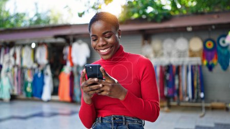 Téléchargez les photos : Femme afro-américaine utilisant smartphone souriant au marché de la rue - en image libre de droit