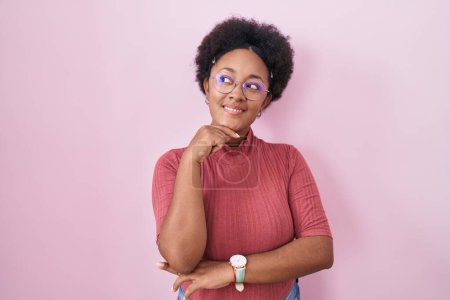 Photo for Beautiful african woman with curly hair standing over pink background with hand on chin thinking about question, pensive expression. smiling and thoughtful face. doubt concept. - Royalty Free Image