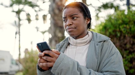 Foto de Mujer afroamericana usando smartphone con expresión seria en el parque - Imagen libre de derechos