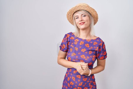 Foto de Mujer caucásica joven con vestido de flores y sombrero de verano con las manos juntas y los dedos cruzados sonriendo relajado y alegre. éxito y optimismo - Imagen libre de derechos