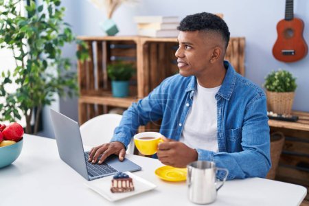 Téléchargez les photos : Young latin man using laptop having breakfast at home - en image libre de droit