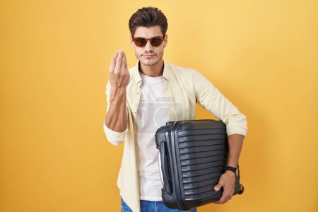 Photo for Young hispanic man holding suitcase going on summer vacation doing italian gesture with hand and fingers confident expression - Royalty Free Image