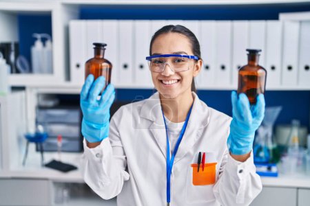 Photo for Young hispanic woman scientist holding bottles at laboratory - Royalty Free Image