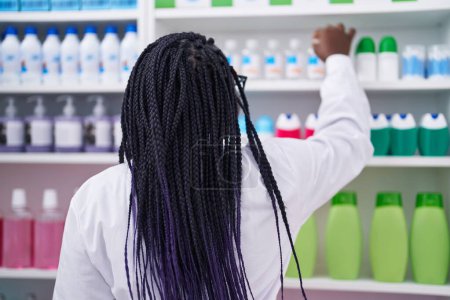 Téléchargez les photos : Pharmacie afro-américaine tenant un produit sur les étagères de la pharmacie - en image libre de droit
