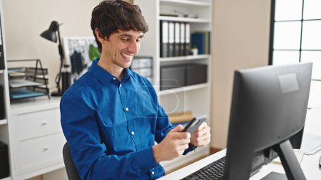 Foto de Joven trabajador de negocios hispano usando computadora y teléfono inteligente en la oficina - Imagen libre de derechos