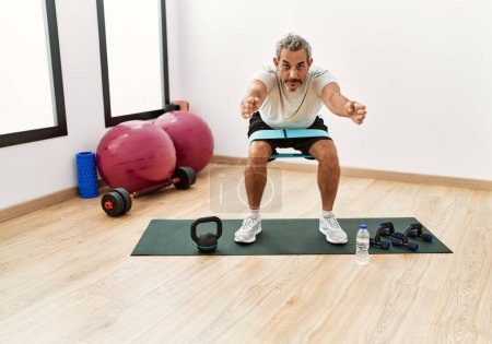 Photo for Middle age grey-haired man training leg exercise at sport center - Royalty Free Image