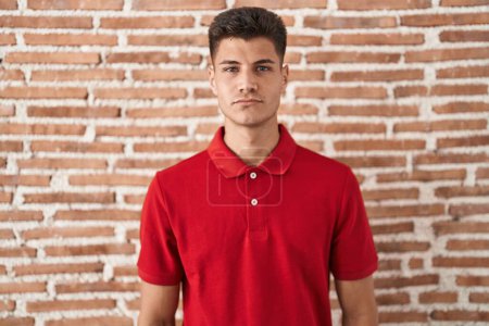 Photo for Young hispanic man standing over bricks wall relaxed with serious expression on face. simple and natural looking at the camera. - Royalty Free Image