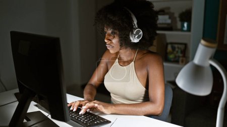 Foto de Trabajadora de negocios afroamericana usando computadora y auriculares en la oficina - Imagen libre de derechos