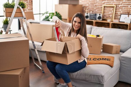 Photo for Young beautiful hispanic woman smiling confident unpacking sneakers of cardboard box at new home - Royalty Free Image