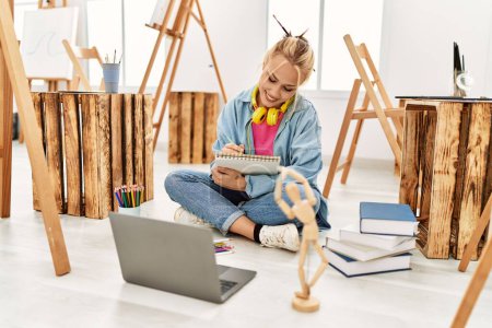 Téléchargez les photos : Jeune artiste femme caucasienne dessin sur ordinateur portable assis sur le sol à l'atelier d'art - en image libre de droit