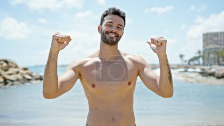 Téléchargez les photos : Jeune homme hispanique touriste en maillot de bain avec geste gagnant à la plage - en image libre de droit