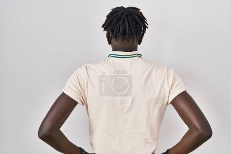 Téléchargez les photos : Homme africain avec dreadlocks debout sur fond isolé debout vers l'arrière regardant loin avec les bras sur le corps - en image libre de droit