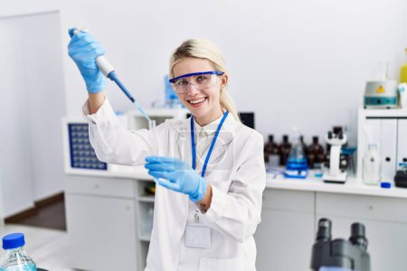 Foto de Joven mujer rubia científica vertiendo líquido en tubo de ensayo en el laboratorio - Imagen libre de derechos