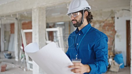 Photo for Young hispanic man architect reading house plans standing at construction site - Royalty Free Image