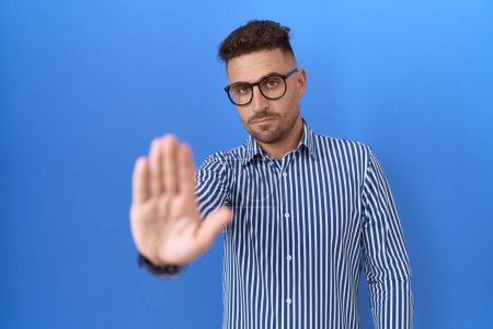 Photo for Hispanic man with beard wearing glasses doing stop sing with palm of the hand. warning expression with negative and serious gesture on the face. - Royalty Free Image