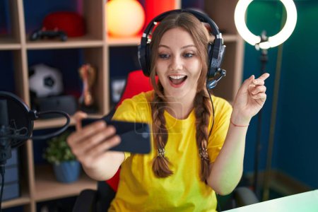 Téléchargez les photos : Jeune femme caucasienne jouant à des jeux vidéo avec smartphone souriant heureux pointant avec la main et le doigt sur le côté - en image libre de droit