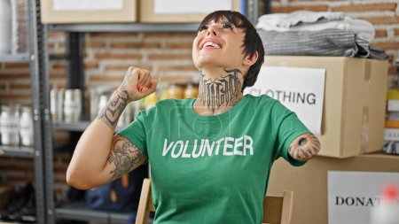Foto de Mujer hispana con brazo amputado voluntaria sonriendo confiada sentada en la mesa con gesto ganador en el centro de caridad - Imagen libre de derechos