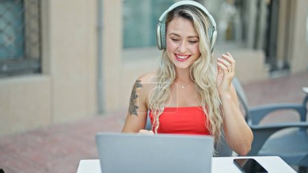 Téléchargez les photos : Jeune femme blonde ayant appel vidéo assis sur la table souriant à la terrasse du café - en image libre de droit
