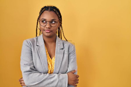 Téléchargez les photos : Femme afro-américaine avec des tresses debout sur fond jaune souriant regardant vers le côté et regardant loin en pensant. - en image libre de droit
