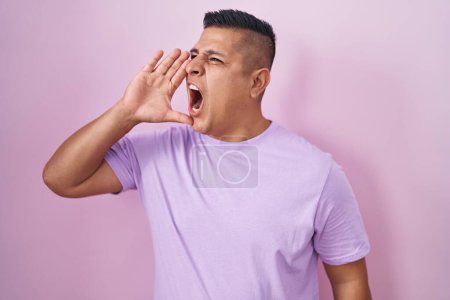 Téléchargez les photos : Jeune homme hispanique debout sur fond rose criant et criant fort à côté avec la main sur la bouche. concept de communication. - en image libre de droit