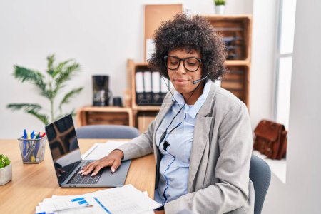 Photo for Black woman with curly hair wearing call center agent headset at the office depressed and worry for distress, crying angry and afraid. sad expression. - Royalty Free Image