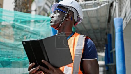 Foto de Hombre afroamericano constructor usando touchpad mirando alrededor en el lugar de construcción - Imagen libre de derechos