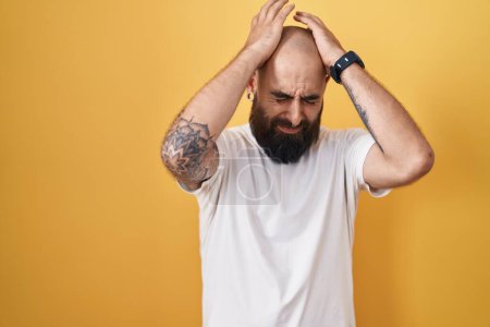 Photo for Young hispanic man with beard and tattoos standing over yellow background suffering from headache desperate and stressed because pain and migraine. hands on head. - Royalty Free Image