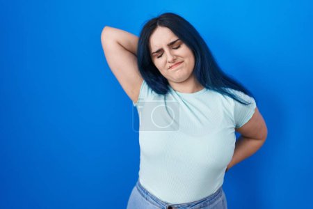 Photo for Young modern girl with blue hair standing over blue background suffering of neck ache injury, touching neck with hand, muscular pain - Royalty Free Image