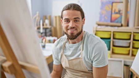 Photo for Young hispanic man artist smiling confident sitting on chair at art studio - Royalty Free Image
