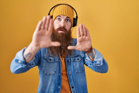 Téléchargez les photos : Homme caucasien à longue barbe écoutant de la musique à l'aide d'écouteurs faisant cadre en utilisant les mains paumes et les doigts, perspective de la caméra - en image libre de droit