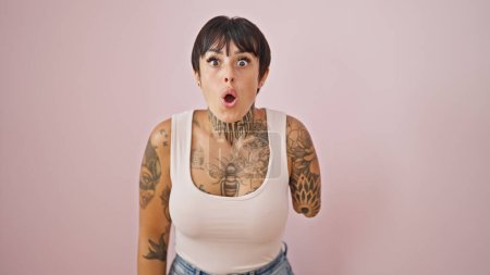 Foto de Mujer hispana con brazo amputado de pie con expresión sorpresa sobre fondo rosa aislado - Imagen libre de derechos