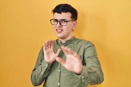 Photo for Non binary person standing over yellow background afraid and terrified with fear expression stop gesture with hands, shouting in shock. panic concept. - Royalty Free Image