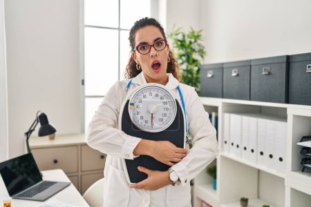 Photo for Young hispanic woman working at dietitian clinic in shock face, looking skeptical and sarcastic, surprised with open mouth - Royalty Free Image