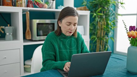 Foto de Mujer hispana madura con cabello gris usando laptop en el comedor - Imagen libre de derechos
